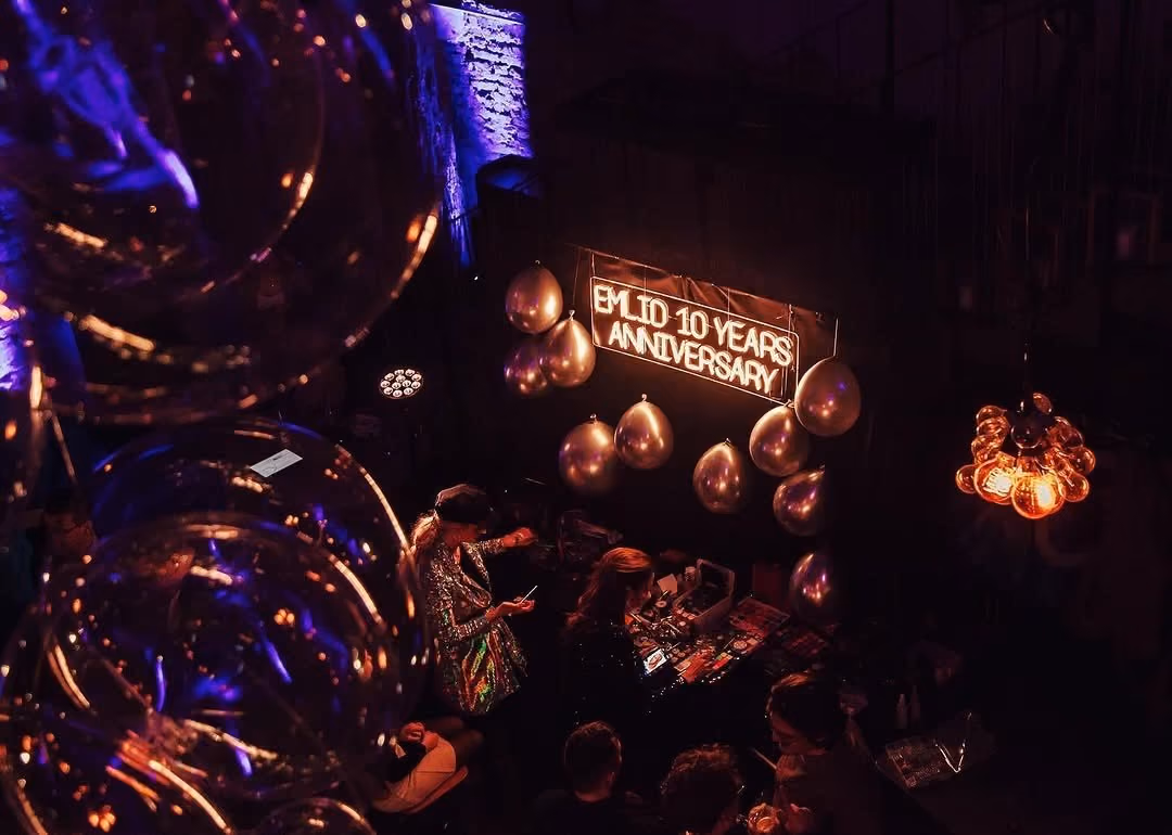 Company anniversary party with a neon sign, balloons and guests at a makeup table, seen from above