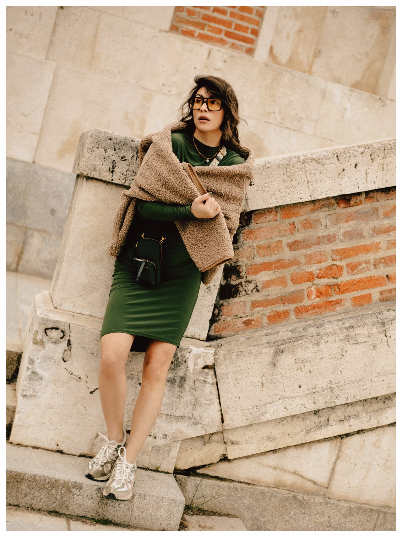 Woman in a green dress and teddy shawl leaning on a stone wall