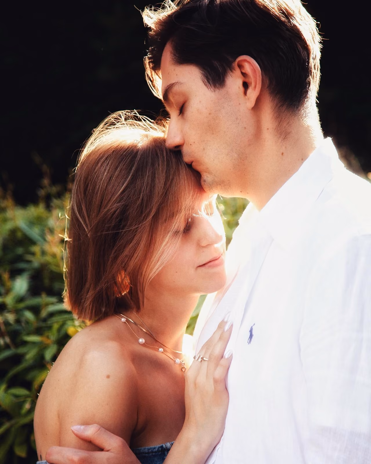 Couple in warm backlight, he kisses her forehead